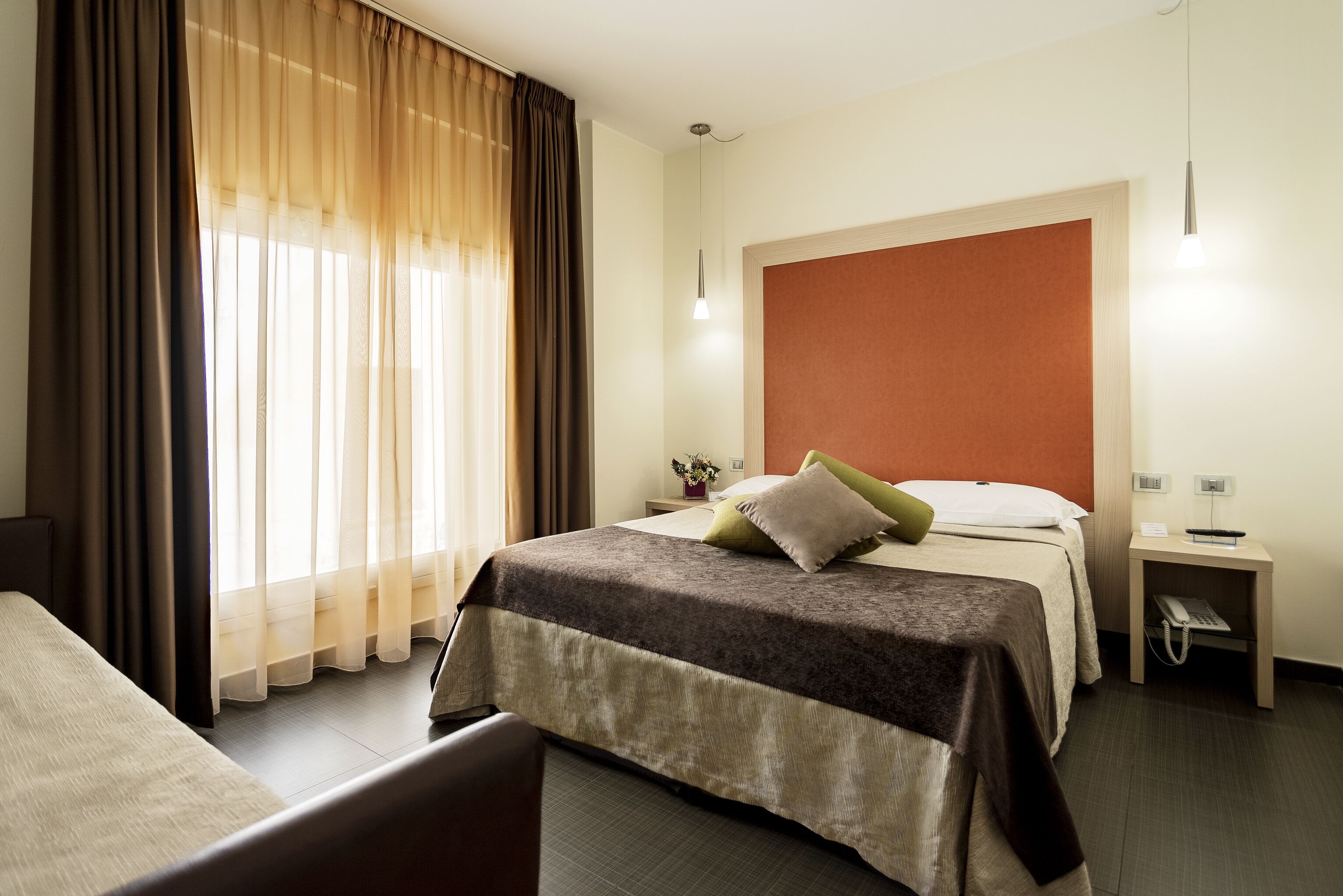 A hotel room with a bed, a bedside table with a lamp, and a window with curtains.