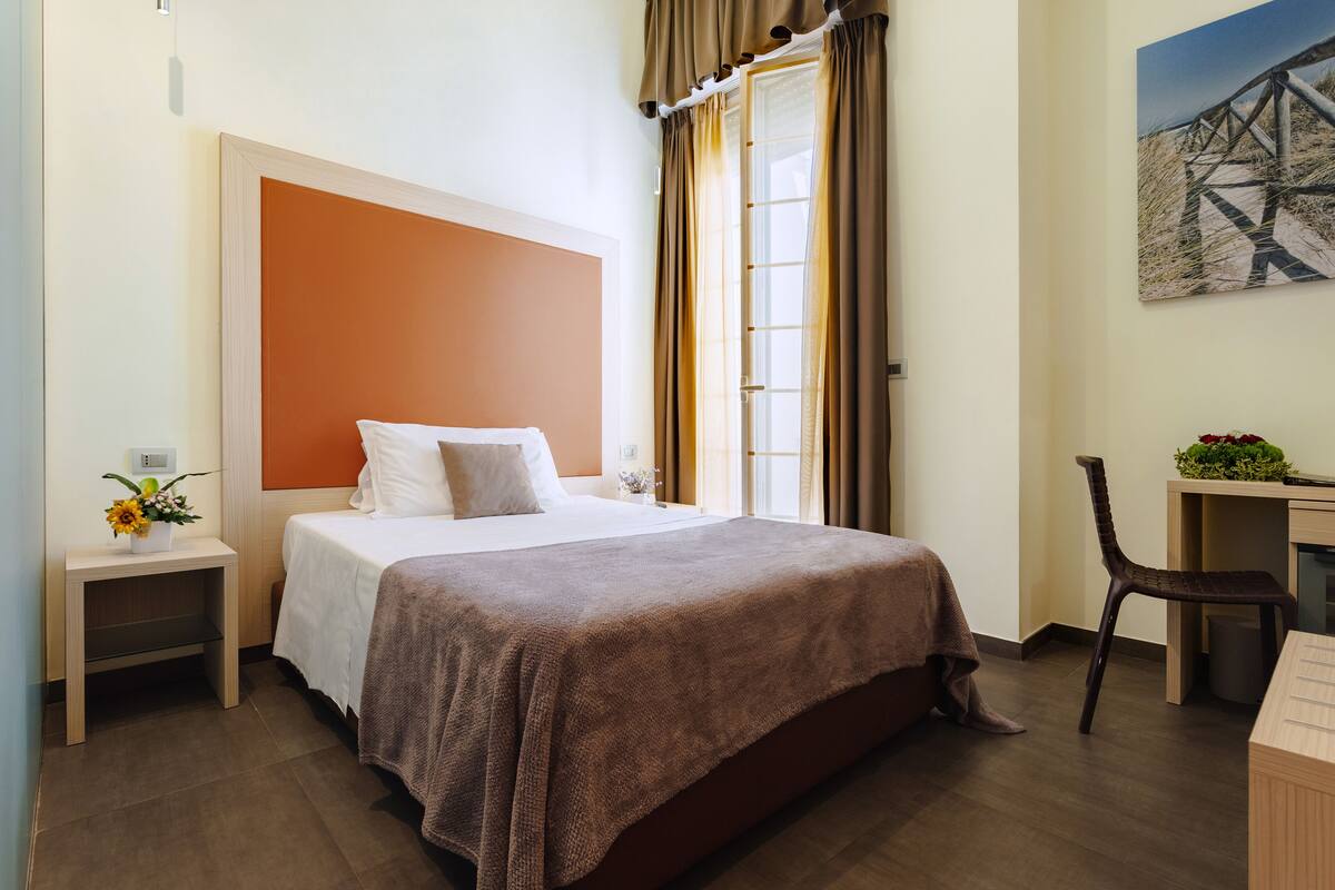 A neatly arranged hotel room with a large bed, a desk, and a chair.