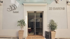 Exterior del hotel 33 Baroni con diseño moderno, que presenta una entrada de vidrio, dos plantas en macetas y un cartel visible con el nombre del hotel.