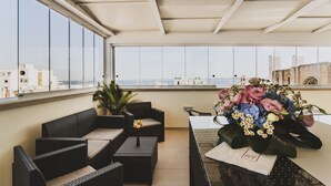 Un balcón con mobiliario de mimbre, una mesa con un arreglo floral y vistas a edificios a lo lejos.