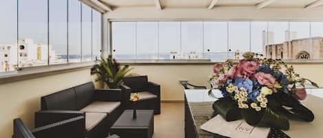 A balcony with wicker furniture, a table with a floral arrangement, and a view of buildings in the distance.