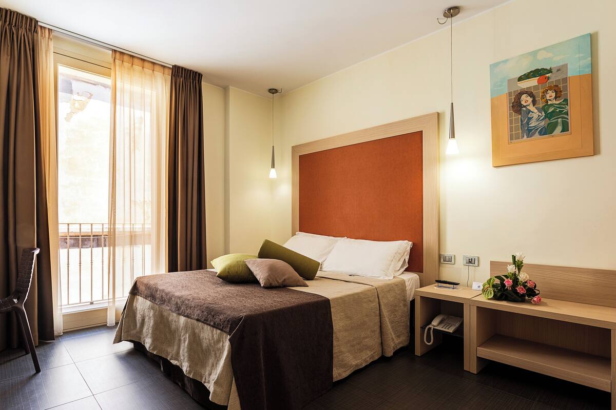 A hotel room with a bed, bedside table, and a painting on the wall.
