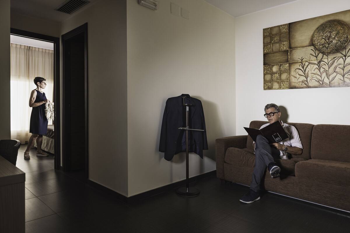 A modern hotel room with a large window, a standing lamp, and a sofa.