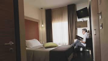 A hotel room with a bed, a desk, a television mounted on the wall, and a window with curtains.