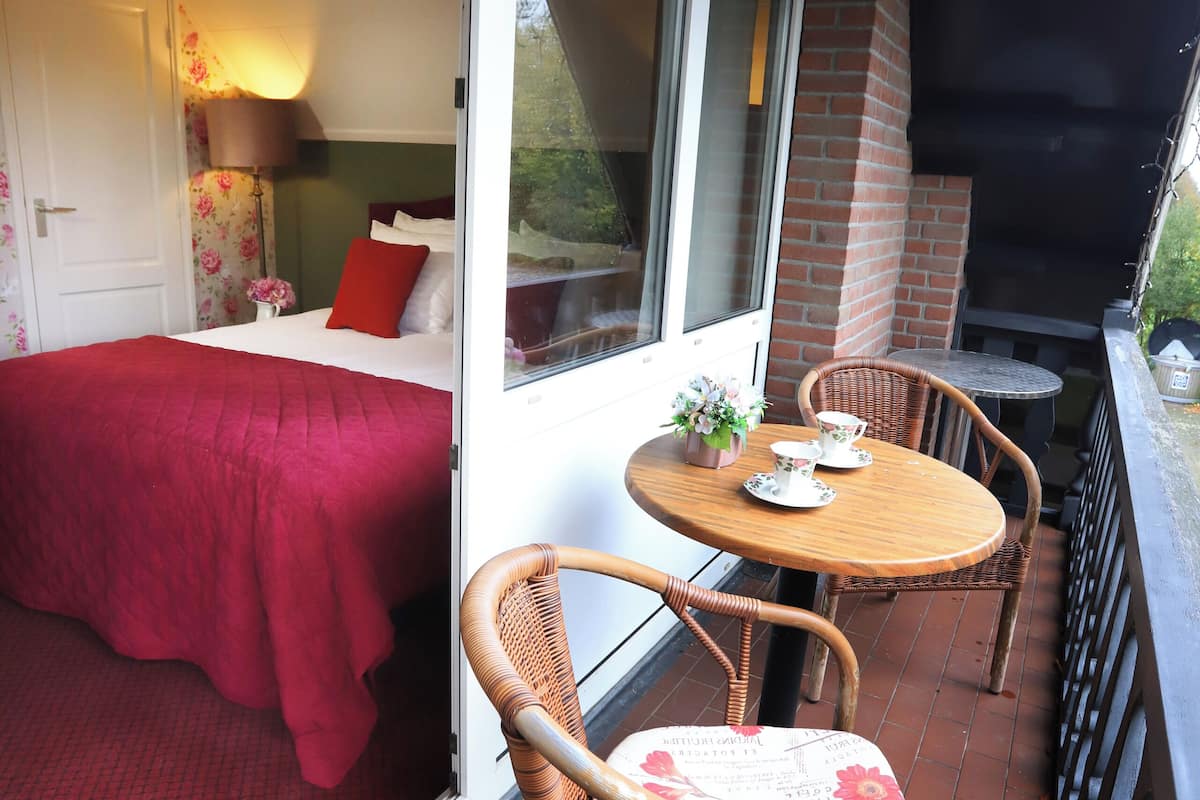 Un balcon avec un lit, des fauteuils en osier et une table agrémentée d’un vase de fleurs.