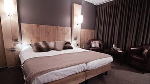 Een hotelkamer met een groot bed, twee nachtkastjes, een stoel en een gordijn.