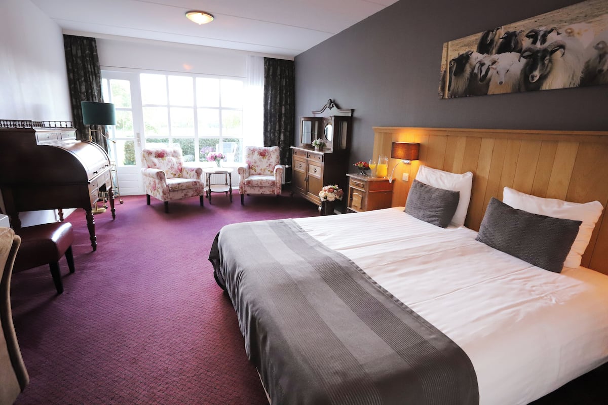 Une chambre d’hôtel avec un grand lit, un bureau, une chaise, une commode et un tableau au mur.