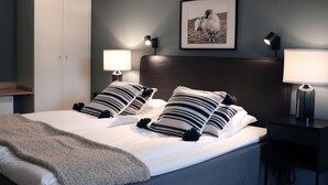 Una cama bien hecha con almohadas a rayas, un cabecero, lámparas de noche y un cuadro en la pared.