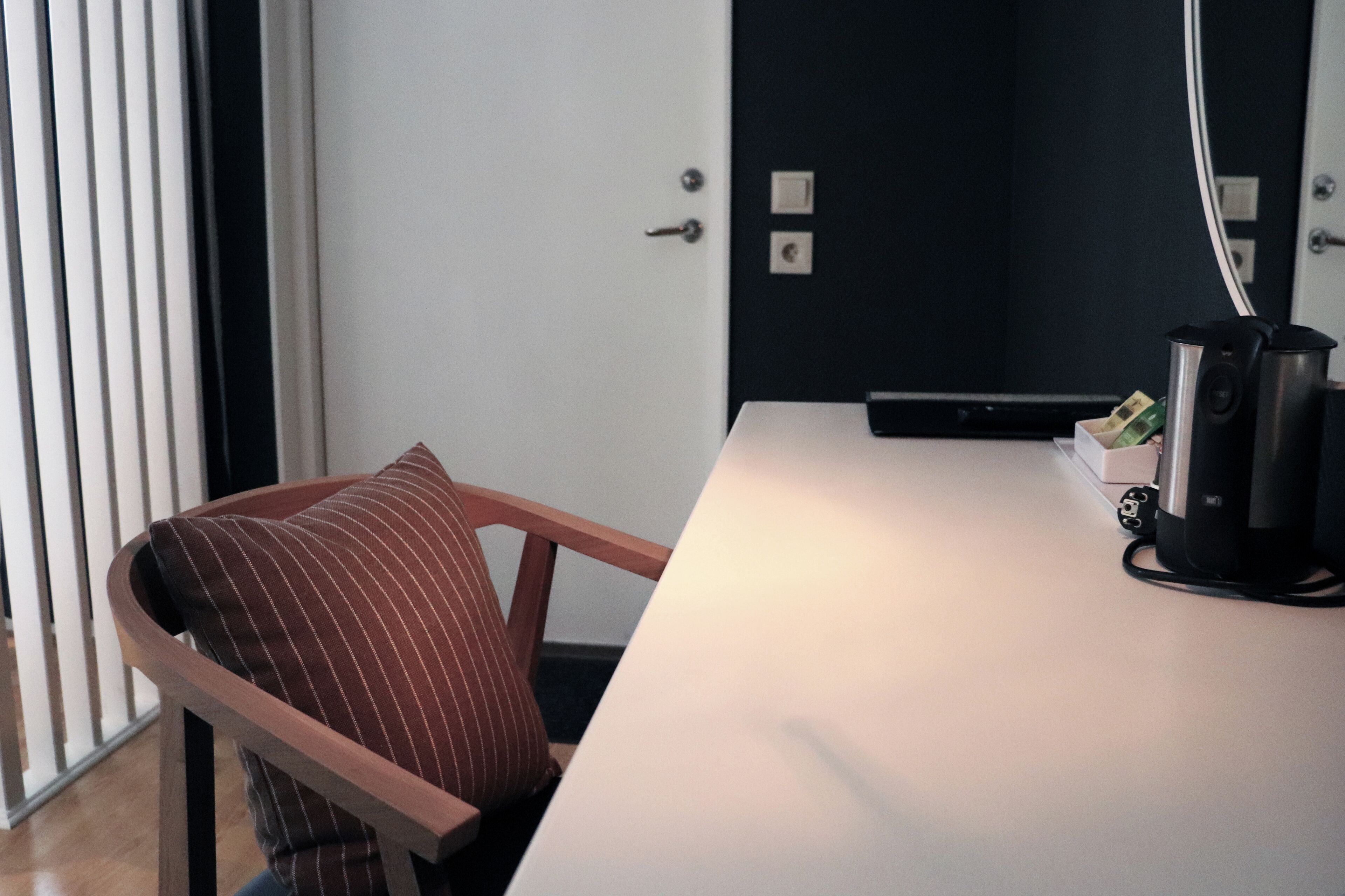 Une cuisine moderne avec un plan de travail blanc, une chaise en bois dotée d’un coussin à rayures et une machine à café.