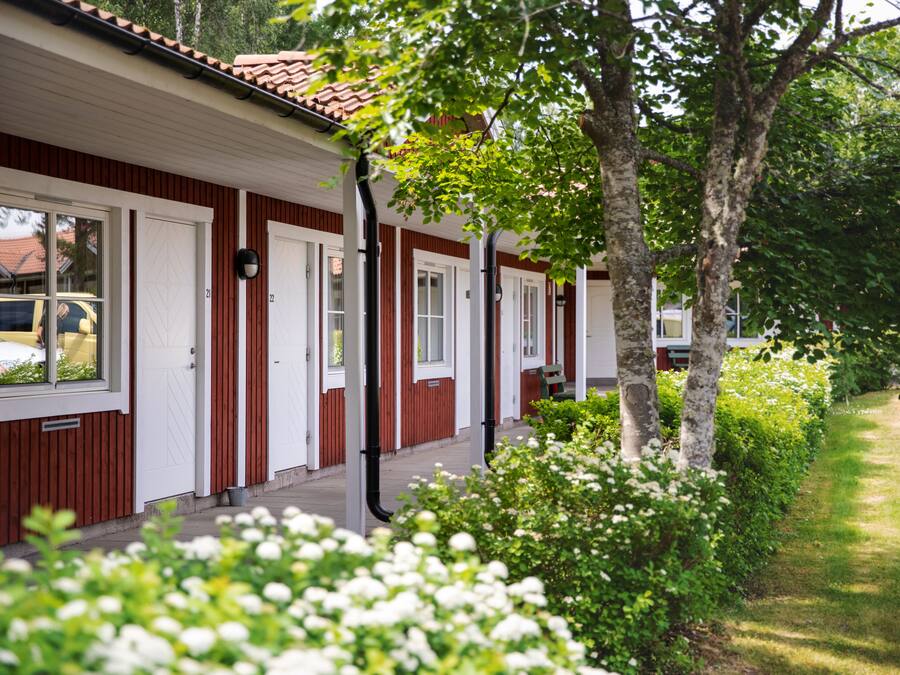 A row of red and white wooden cabins with white doors and windows, surrounded by greenery and trees.