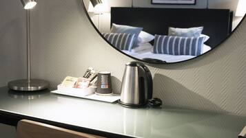 Una habitación de hotel moderna con un espejo redondo, un escritorio con lámpara, una tetera y una silla.