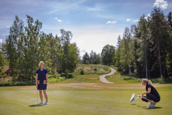 A golf course with a clear path, trees, and a distant road. - Hotell Miskarp (Mjolby)