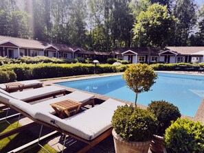 A swimming pool with lounge chairs and potted plants, surrounded by neatly trimmed hedges and a row of houses in the background. - Hotell Miskarp (Mjolby)