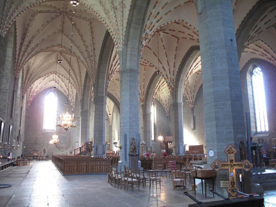 Un vaste intérieur de cathédrale, avec de hauts plafonds en voûte, des rangées de bancs en bois et un autel central.
