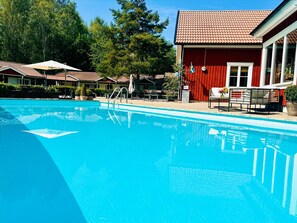A swimming pool with lounge chairs and a red building with a flag. - Hotell Miskarp (Mjolby)