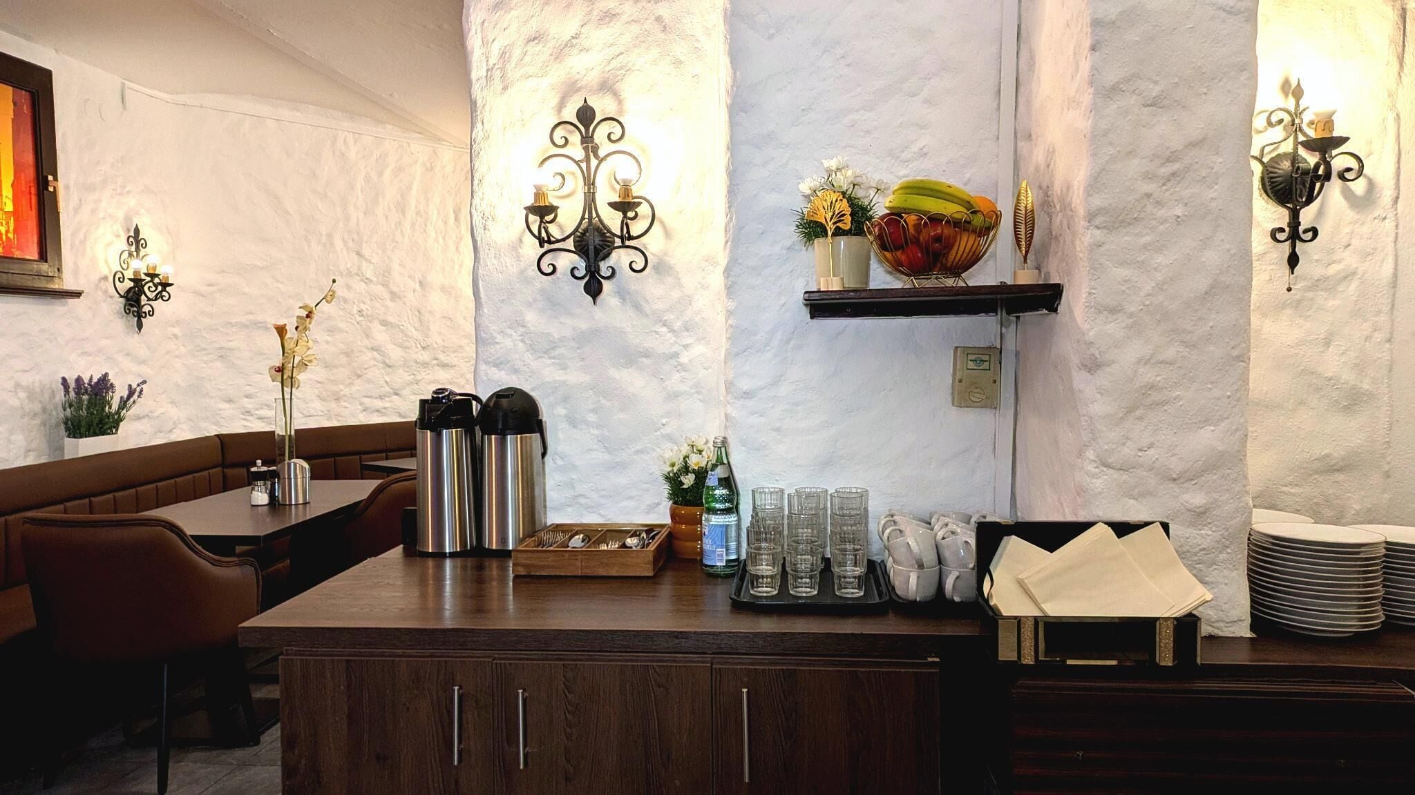 L’intérieur d’un restaurant, avec un comptoir en bois, des sièges, des appliques murales décoratives et un panier de fruits posé sur une étagère.