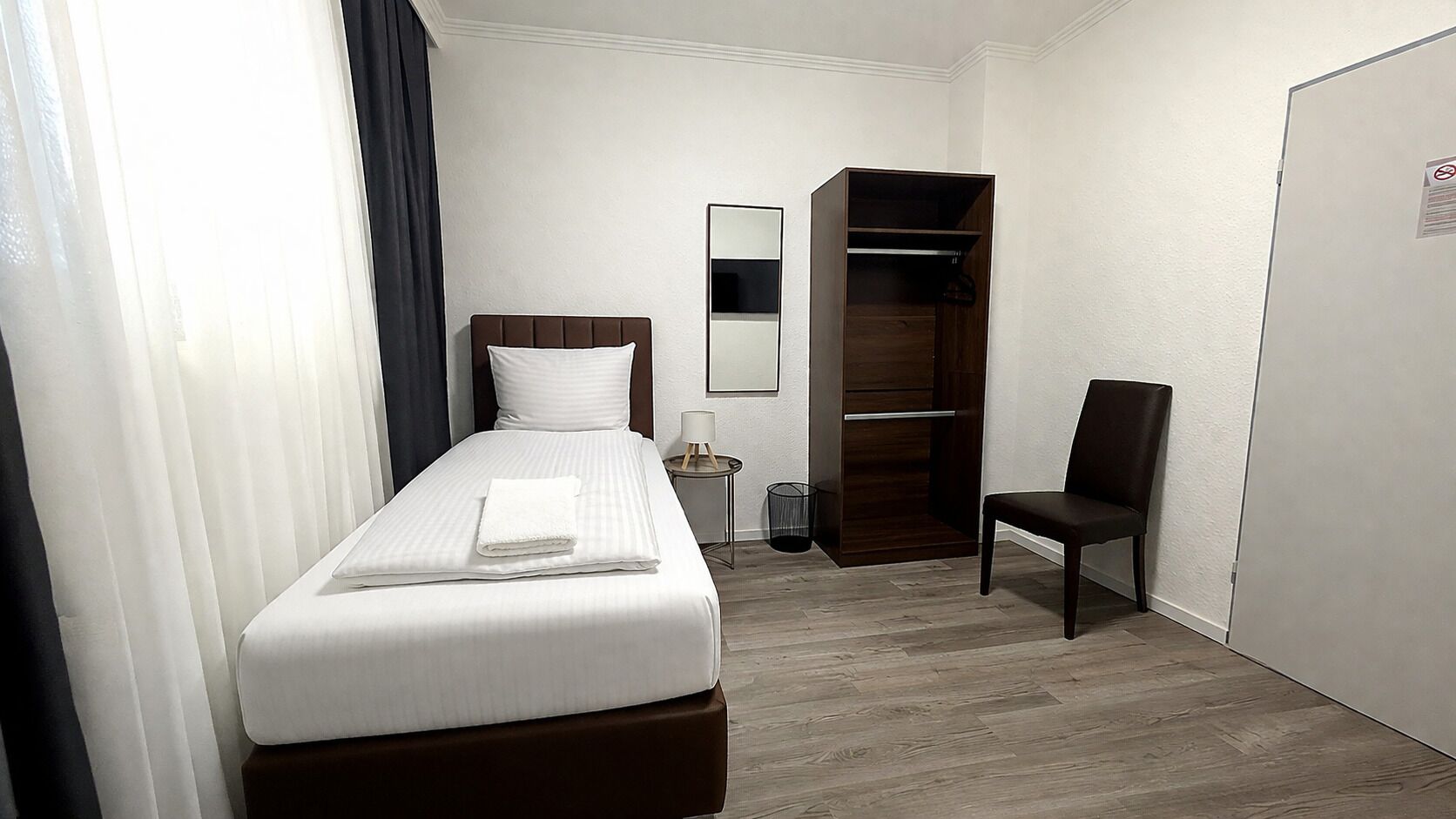 Ein Hotelzimmer mit Bett, Stuhl, Kleiderschrank, Nachttisch und Spiegel.