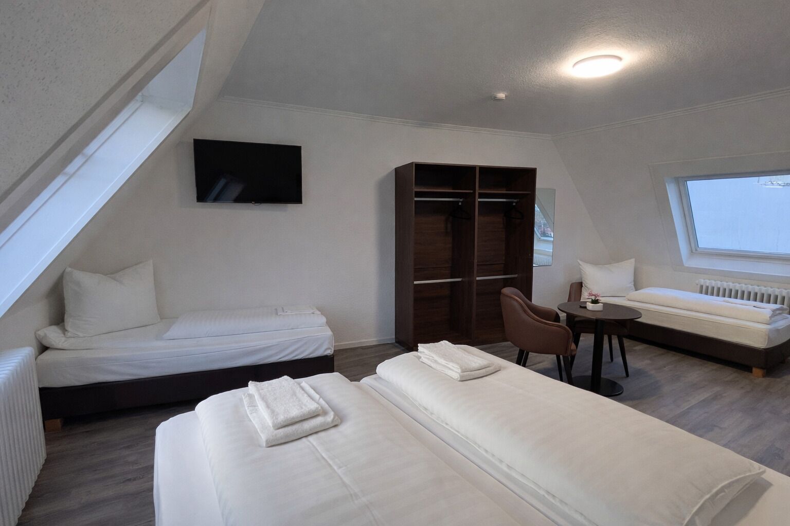 A room with two beds, a desk, a chair, a TV, and a window.