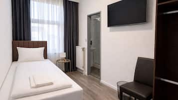 Una habitación de hotel con cama, una silla, un televisor, una ventana con cortinas y una puerta que da a un baño.