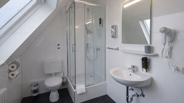 Un baño moderno con cabina de ducha de vidrio, un inodoro, un lavabo y un secador de pelo montado en la pared.