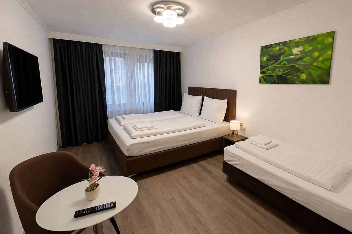 A hotel room with a bed, a smaller bed, a desk with a remote, a chair, and a painting on the wall.