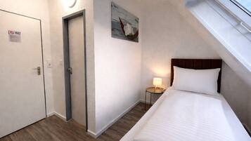 Ein Hotelzimmer mit Bett, Nachttisch mit Lampe, Tür und einem Gemälde an der Wand.