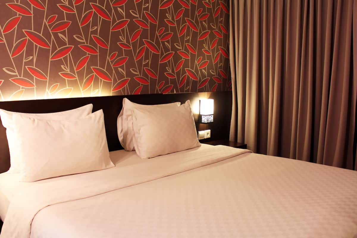A hotel room with a large bed, two pillows, a nightstand with a lamp, and a wall with a leaf pattern.