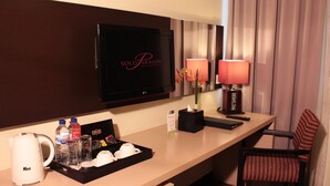 A hotel room with a TV, a minibar, a coffee maker, a tray with cups and a bottle, a remote control, and a chair. - Solo Paragon Hotel & Residences (Surakarta)