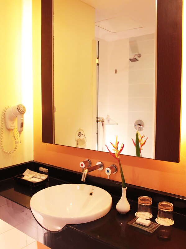 A bathroom with a white sink, a mirror, a hairdryer, and a vase with flowers.