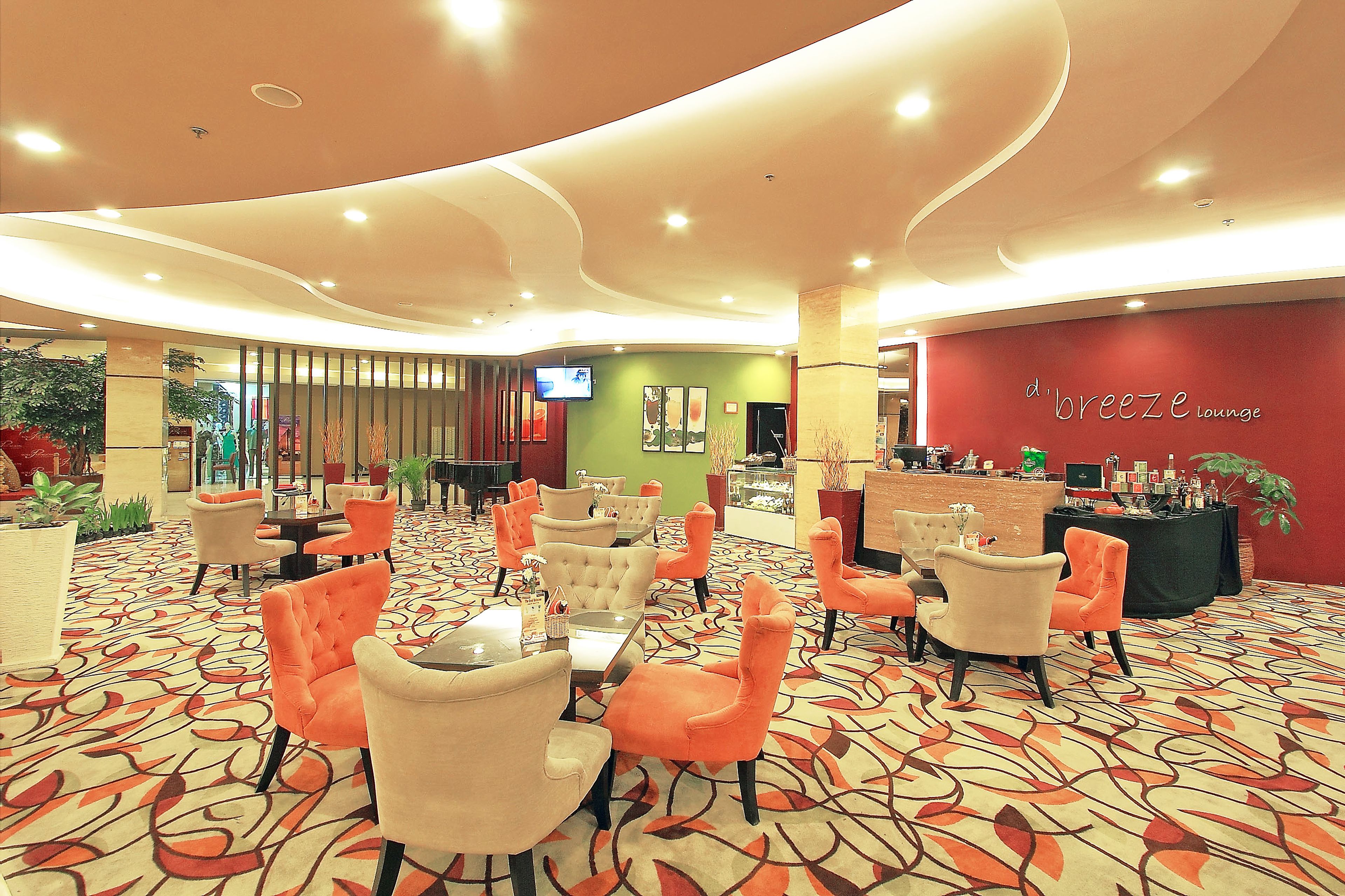 A lounge area with orange and beige chairs, a patterned carpet, and a red wall with 'd'Breeze Lounge' signage.