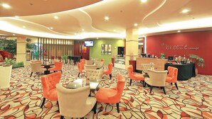 A lounge area with orange and beige chairs, a patterned carpet, and a red wall with 'd'Breeze Lounge' signage. - Solo Paragon Hotel & Residences (Surakarta)