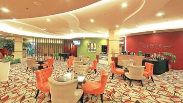 A lounge area with orange and beige chairs, a patterned carpet, and a red wall with 'd'Breeze Lounge' signage.