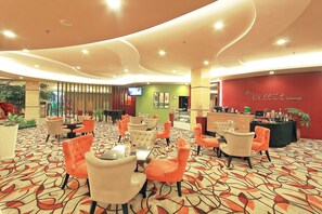 A lounge area with orange and beige chairs, a patterned carpet, and a red wall with 'd'Breeze Lounge' signage. - Solo Paragon Hotel & Residences (Surakarta)