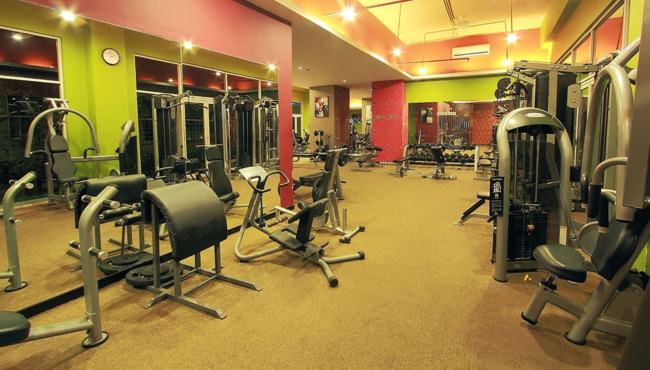 A gym with various exercise machines, mirrors, and a clock on the wall.
