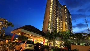 A high-rise hotel with multiple floors, a well-lit entrance, and a parking area with cars. - Solo Paragon Hotel & Residences (Surakarta)