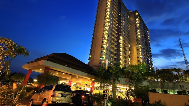 A high-rise hotel with multiple floors, a well-lit entrance, and a parking area with cars. - Solo Paragon Hotel & Residences (Surakarta)