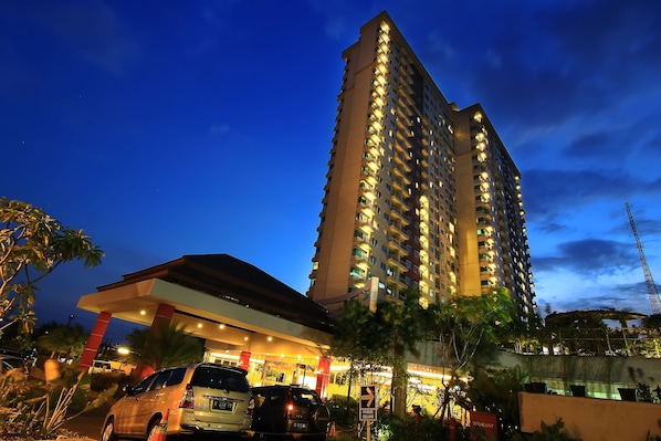 A high-rise hotel with multiple floors, a well-lit entrance, and a parking area with cars. - Solo Paragon Hotel & Residences (Surakarta)