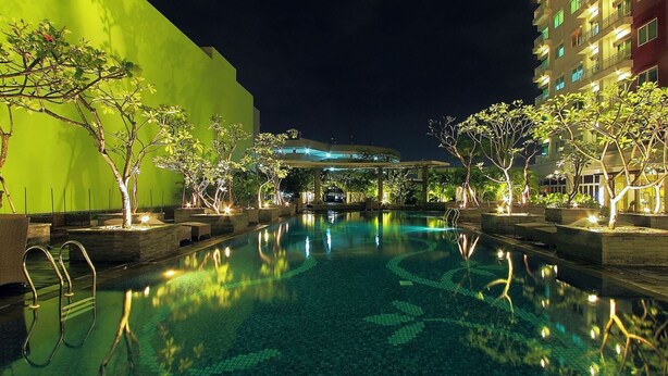 A nighttime swimming pool area with a clear pool, surrounding trees, and a building in the background. - Solo Paragon Hotel & Residences (Surakarta)