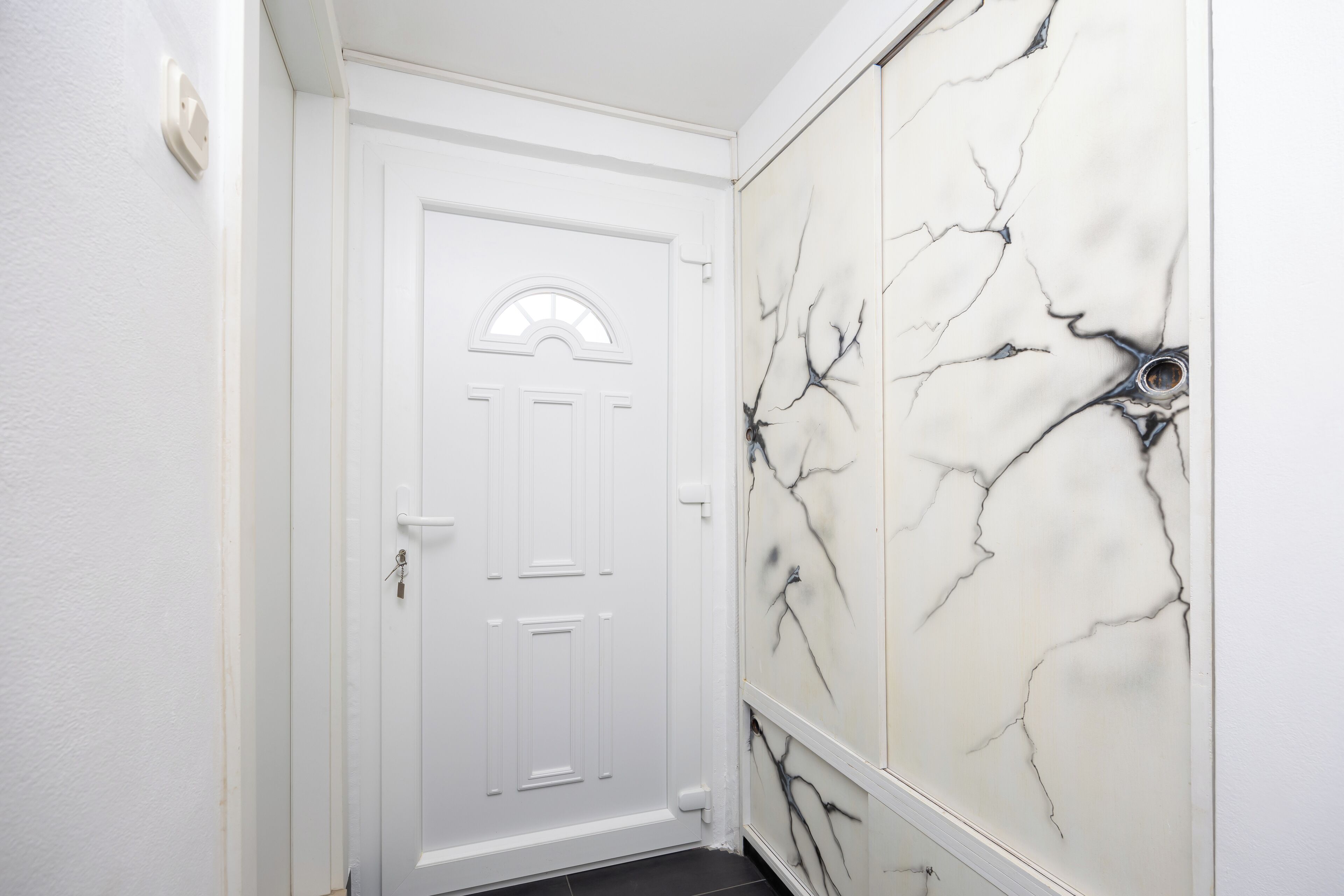 A hallway with a white door and a wall with a marble-like design.