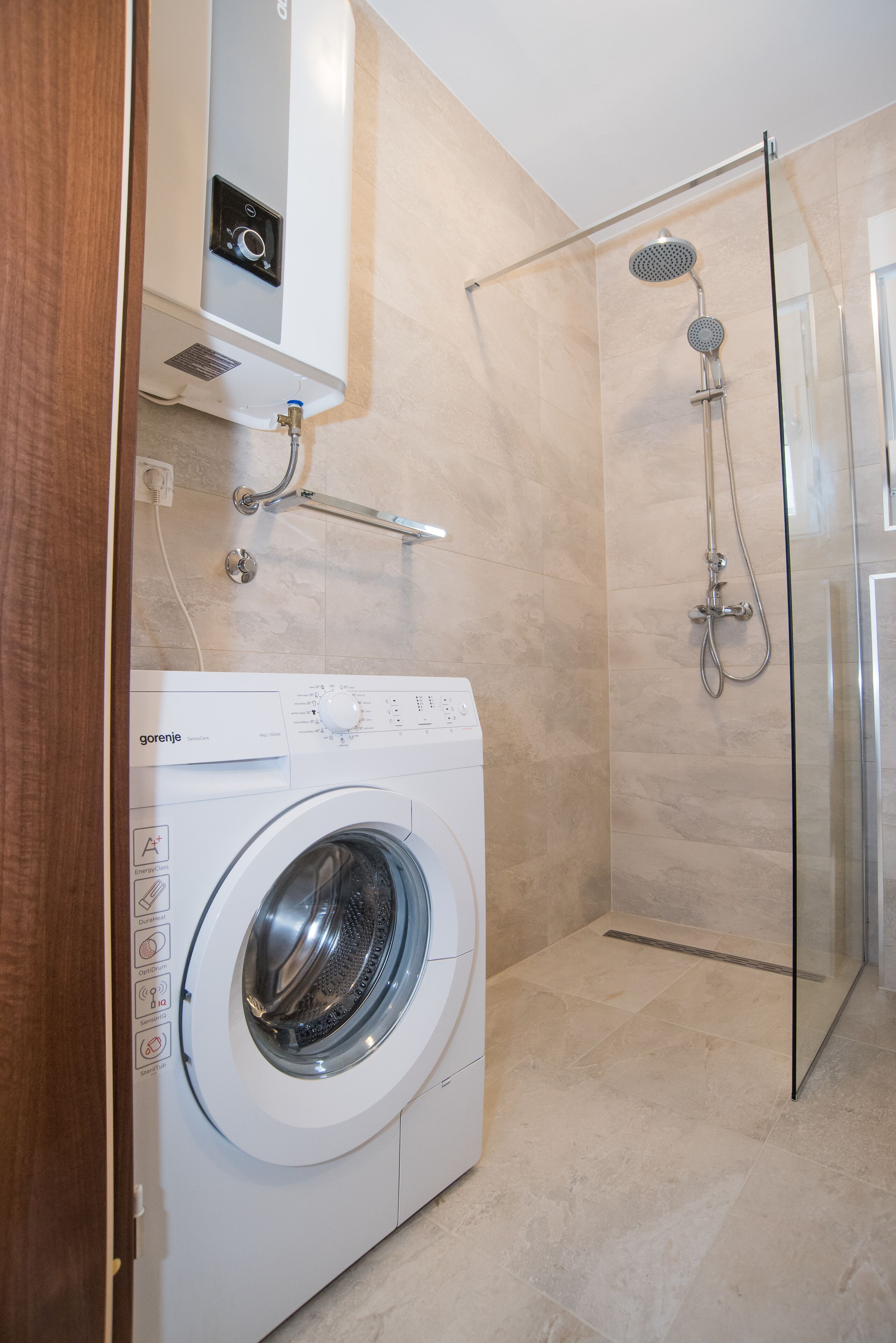 A modern bathroom with a built-in washing machine, a glass shower enclosure, and a towel rack.