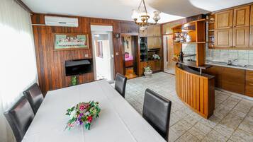 Un coin repas avec une table blanche, des chaises et un arrangement floral en guise de décoration centrale. On y trouve également un coin cuisine avec des meubles en bois et un évier.