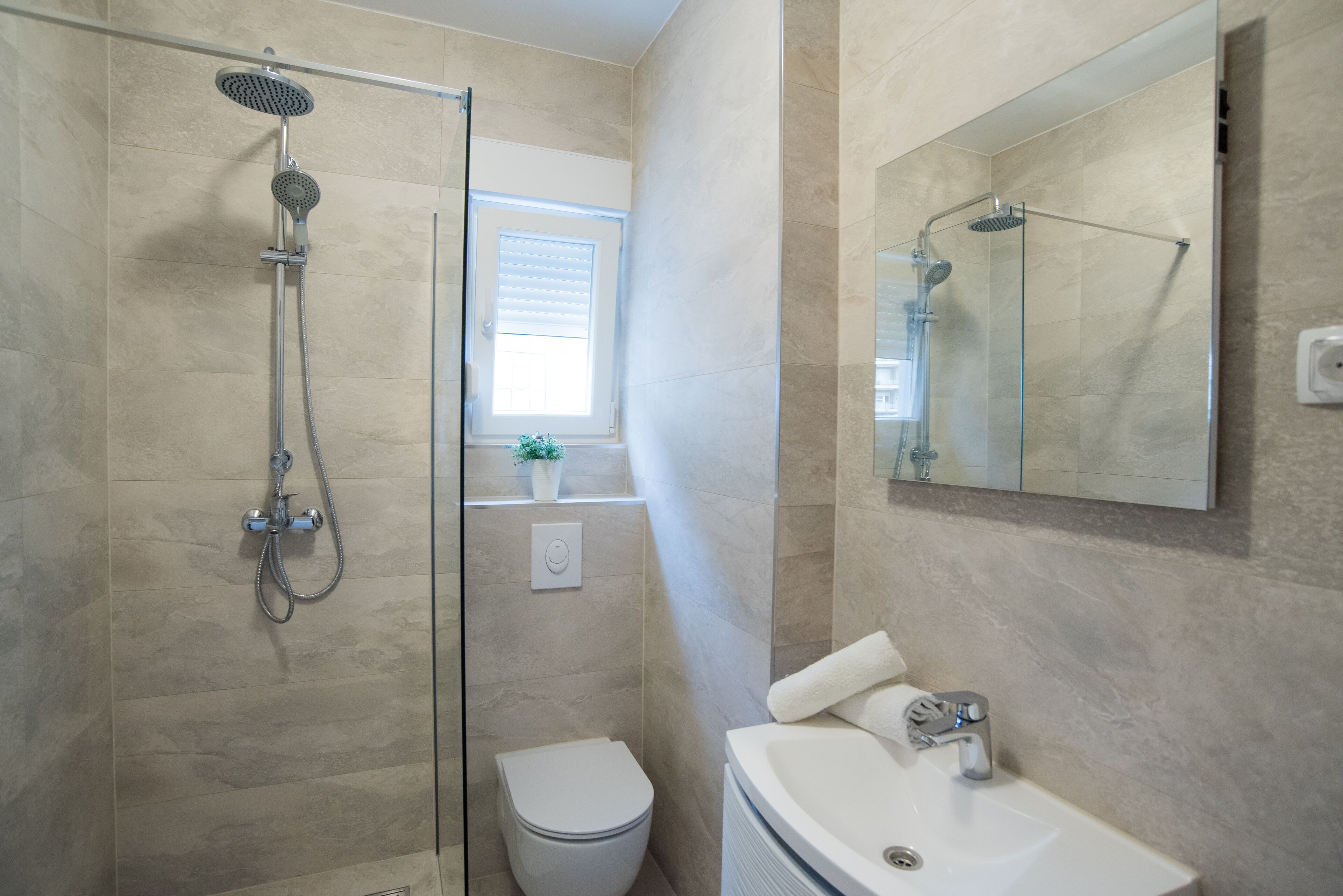 A bathroom with a glass-enclosed shower, a white toilet, and a sink with a mirror above it.