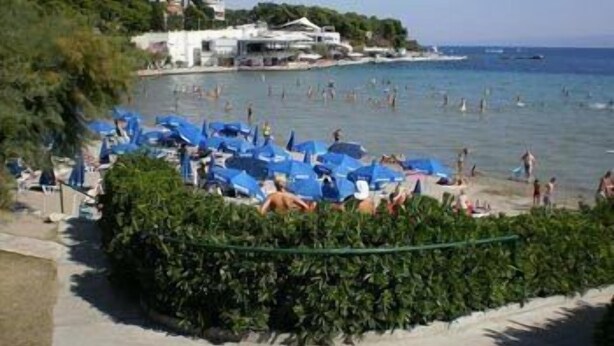 Une plage avec des parasols bleus et des gens qui se baignent.