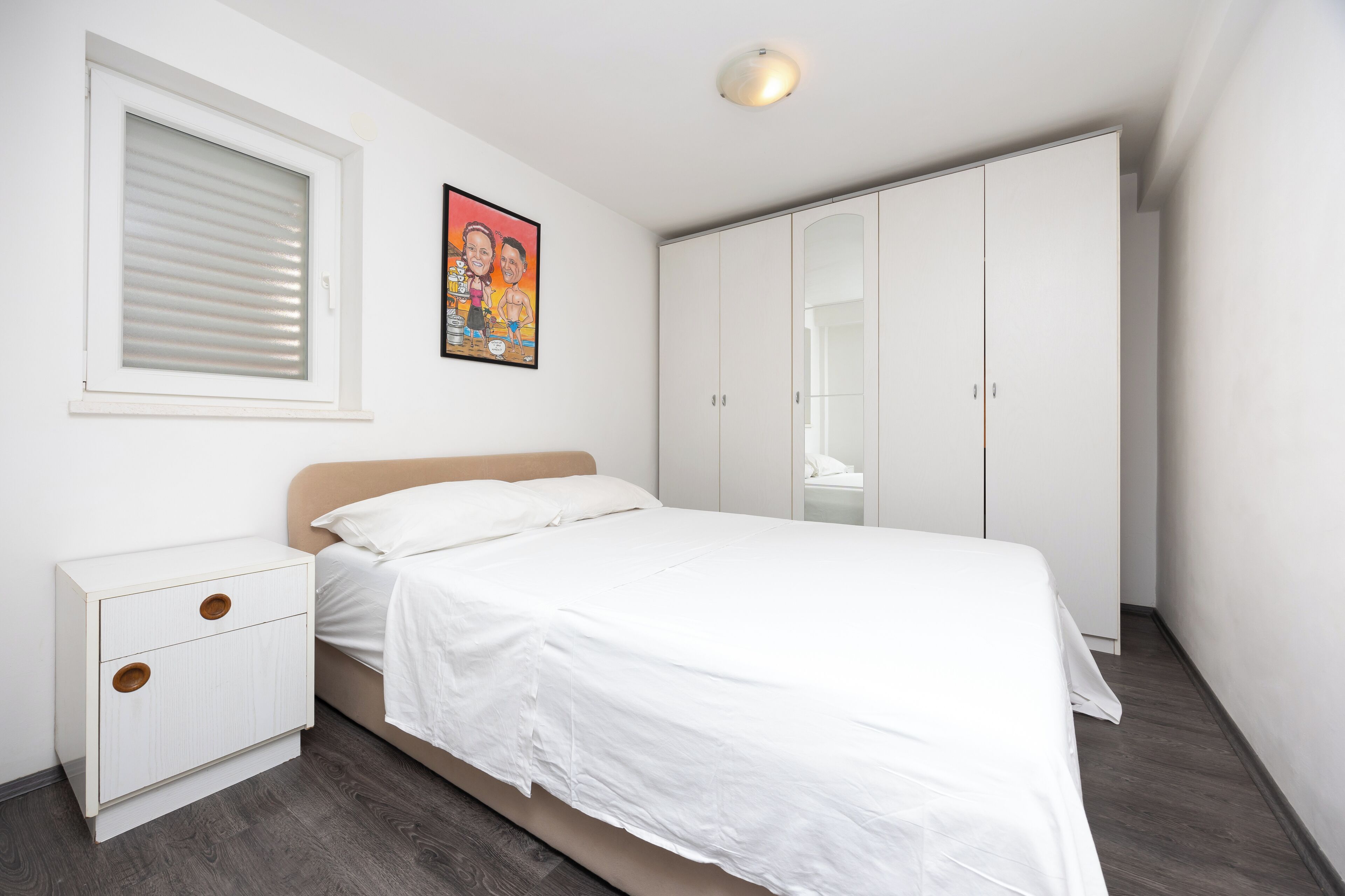 Un dormitorio con cama, mesita de noche, armario y ventana con persianas.