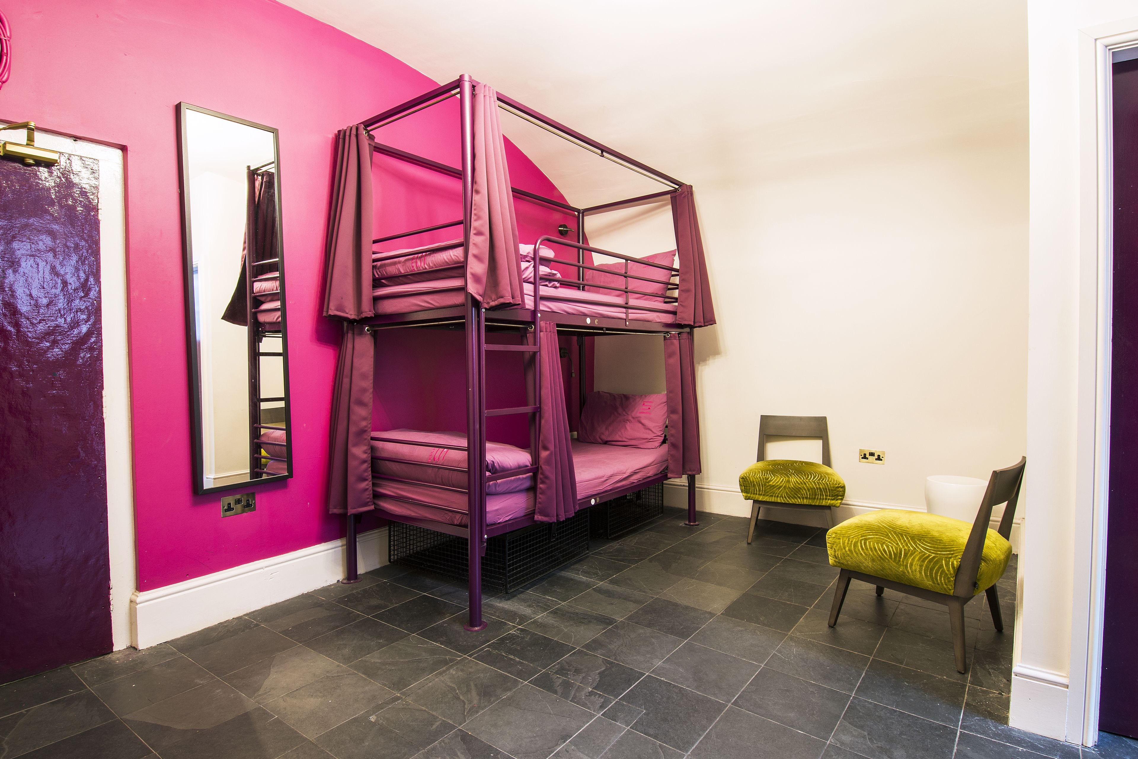 Ein Zimmer mit einem Etagenbett, einem Stuhl, einem Spiegel und einer Tür.