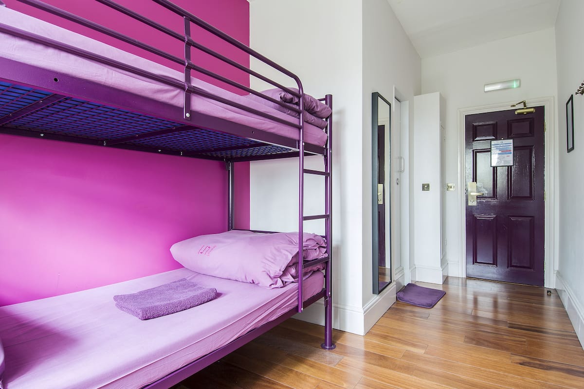 A bunk bed room with a purple mattress and pillows, a wooden floor, and a door with a sign.