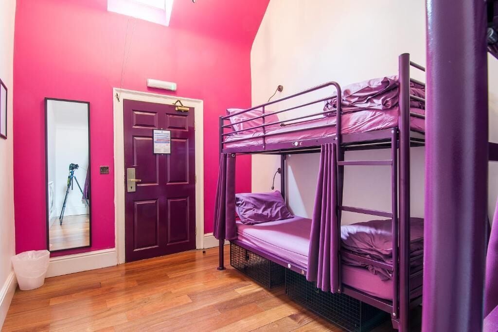Een kamer met twee stapelbedden, een houten vloer, een paarse deur en een spiegel.