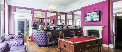 A bar area with a pool table, bar stools, and a fireplace.