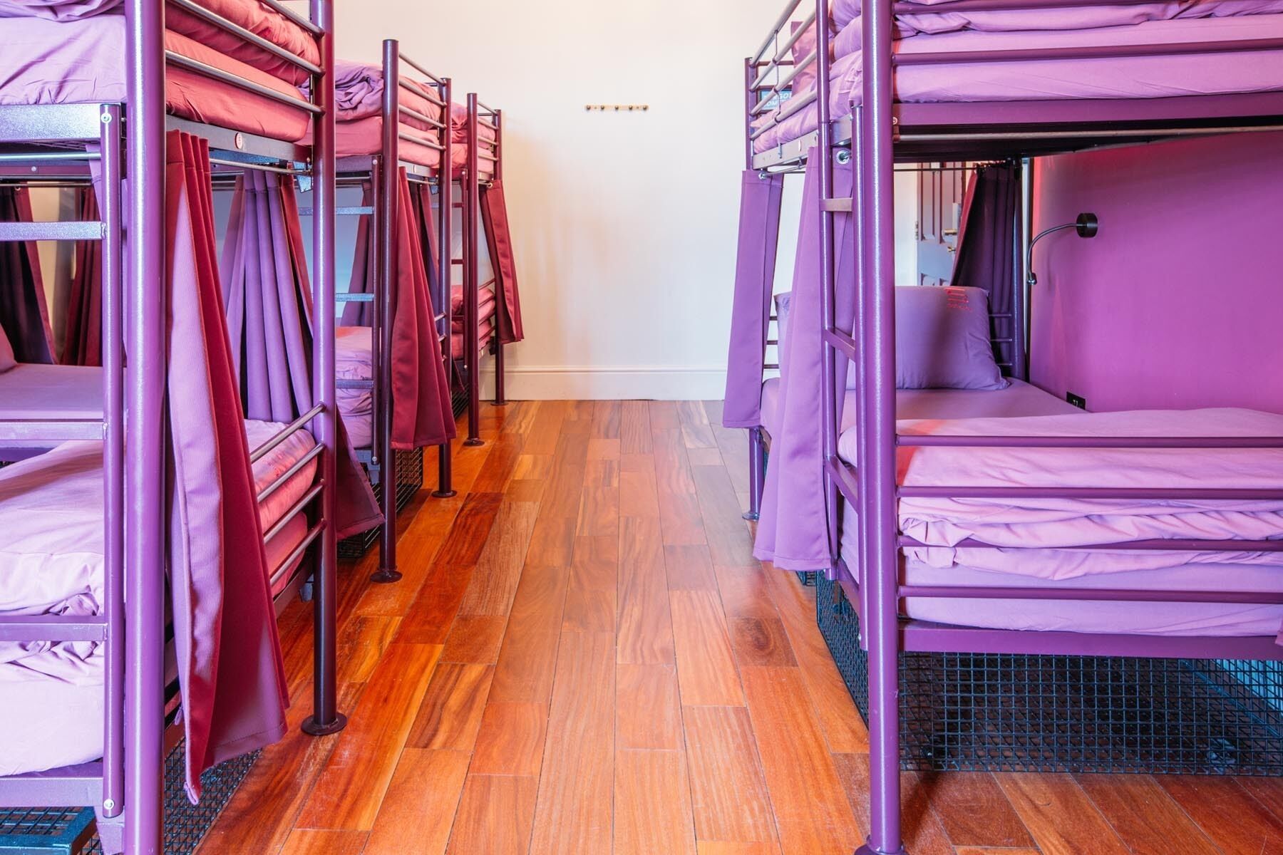 A row of bunk beds with purple bedding in a room with wooden flooring.
