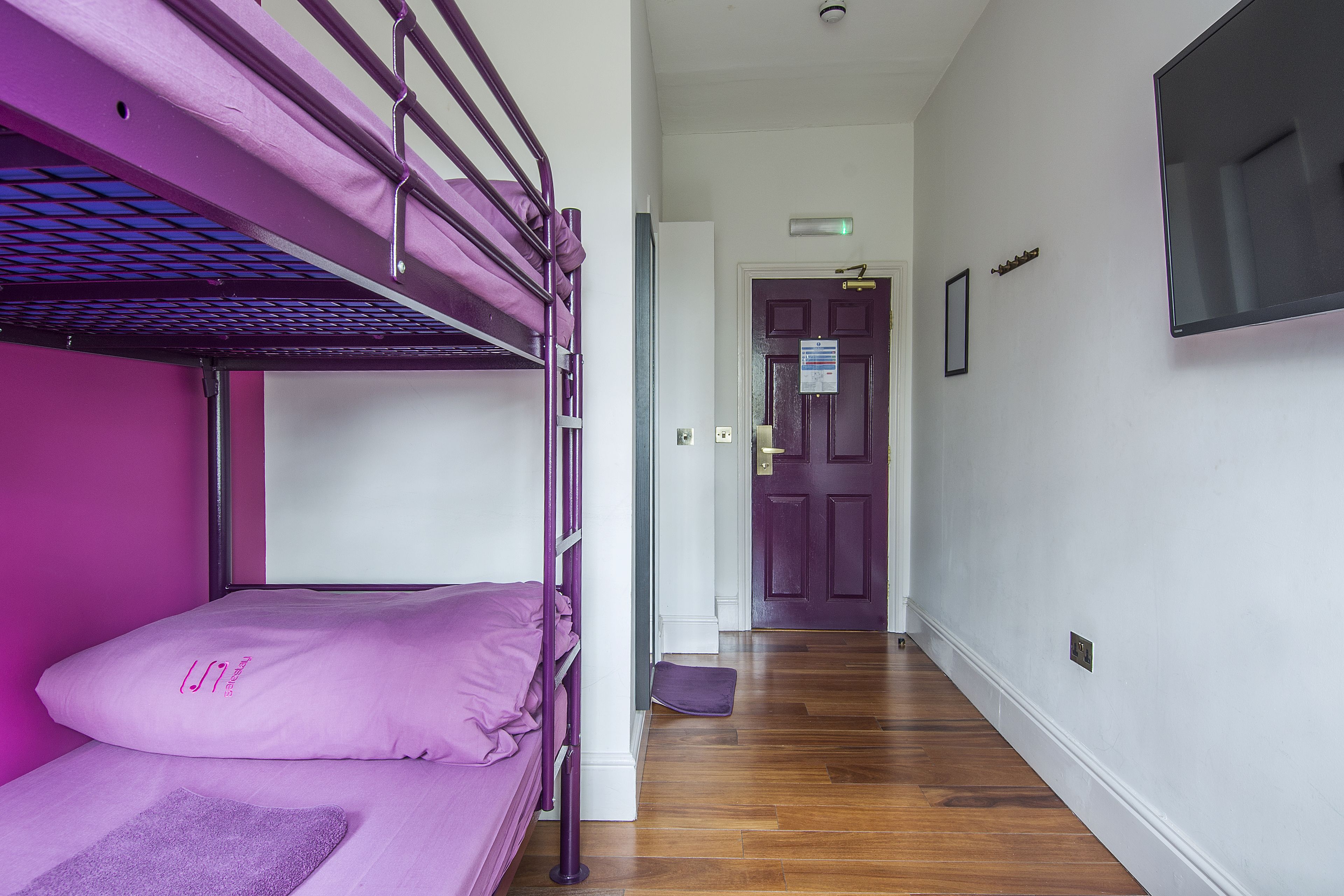 A bunk bed with a purple headboard and footboard, a wooden floor, and a door with a sign in the hallway.